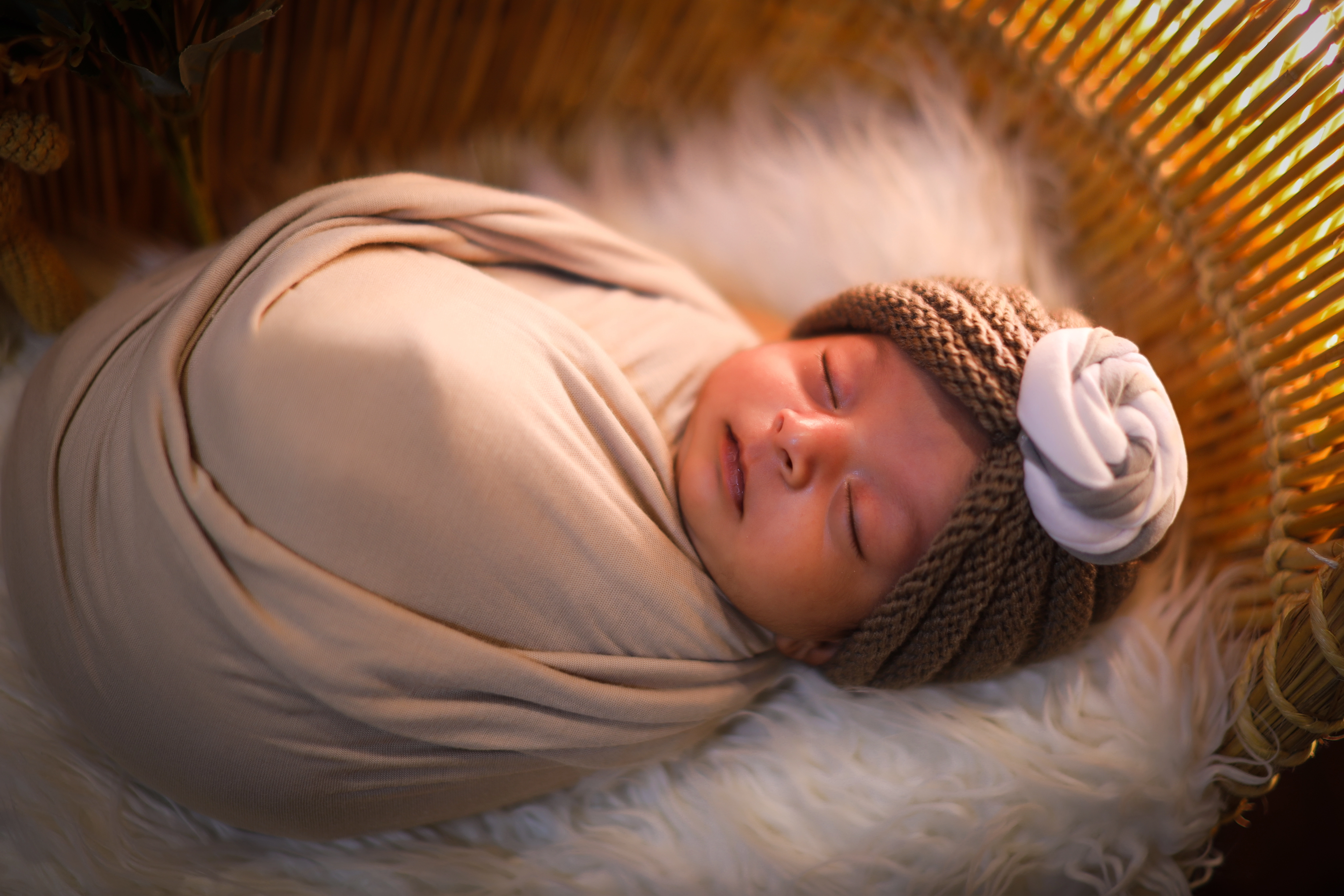 Newborn baby wrapped in cream organic fabric with knit bonnet sleeping in a basket